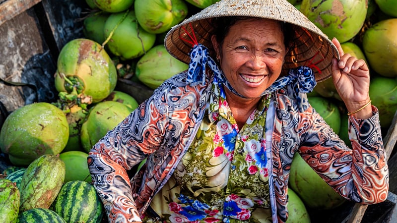 fruit vendor surrounded by whole green coconuts and watermelons, a scene highly characteristic of traditional floating markets in Southeast Asia.