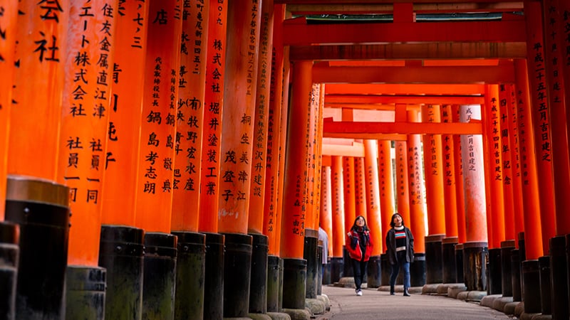 Kyoto, Japan: Young women walking on walkway surrounded by red gates in Fushimi Inari shrine.