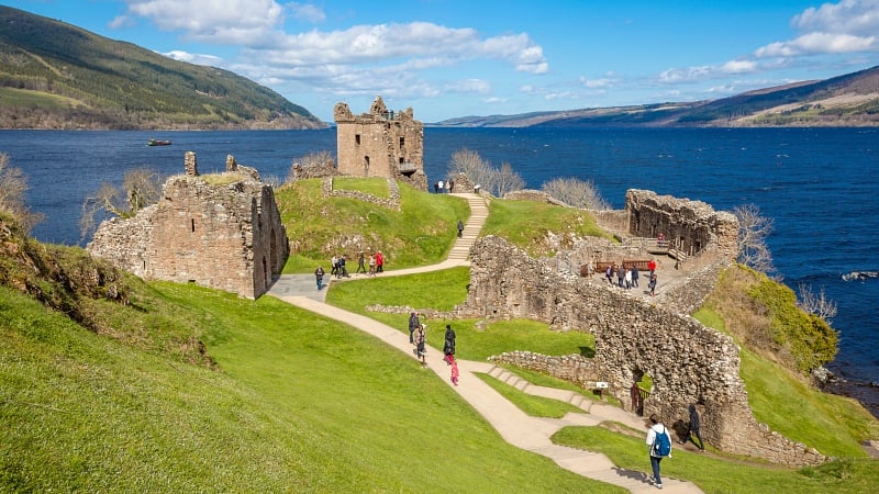 The image displays the medieval ruins of Urquhart Castle, located on the shores of Loch Ness in the Scottish Highlands.
