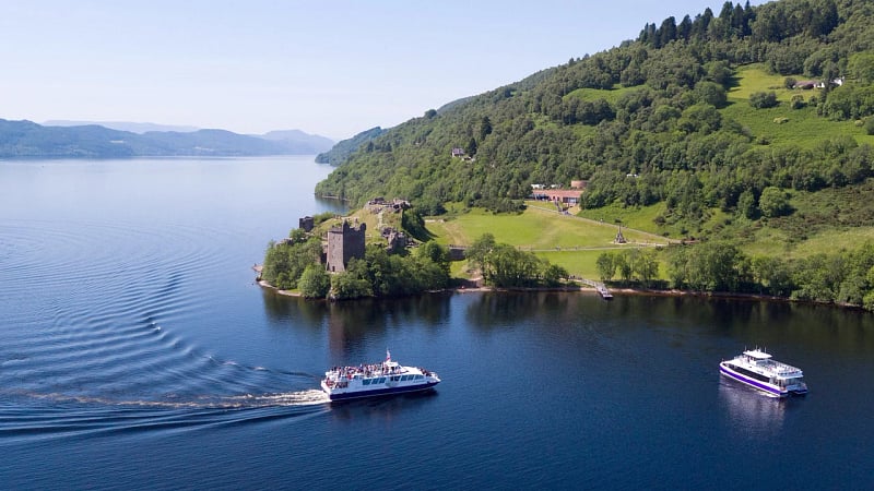 This image shows the historic ruins of Urquhart Castle positioned on a rocky promontory overlooking the deep waters of Loch Ness in the Scottish Highlands.