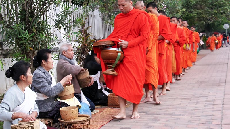 Buddhist monks wearing traditional saffron robes while carrying alms bowls to collect morning offerings
