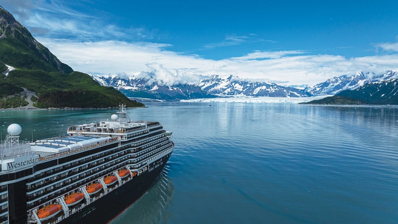 This image shows a premium Vista-class cruise ship. It is pictured here navigating through the icy waters of a tidal glacier destination in Alaska (such as Glacier Bay National Park or the Hubbard Glacier), surrounded by towering snow-capped mountains.