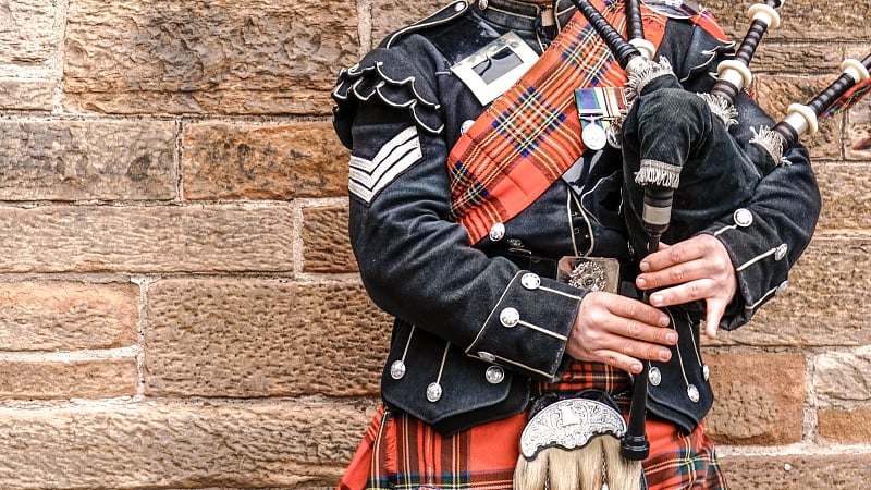 Scottish bagpiper dressed in full traditional Highland military regimental uniform, performing on the Great Highland bagpipes.