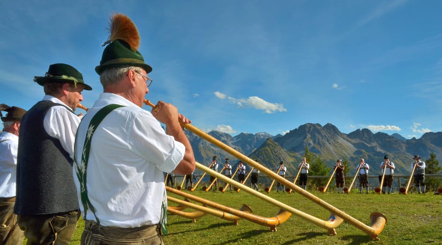 Group of musicians playing the alphorn (also known as the alpenhorn or alpine horn), a traditional wooden wind instrument primarily associated with the Swiss Alps and surrounding mountain regions