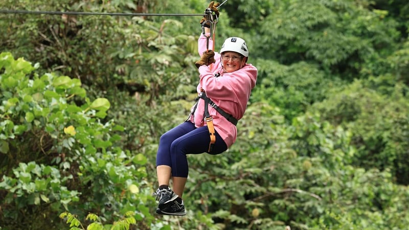 This image shows a person ziplining (canopy tour) through a lush tropical rainforest canopy.