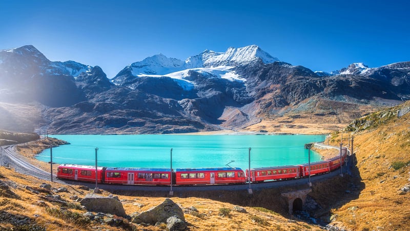 The iconic Bernina Express passing along the shores of Lago Bianco (White Lake) in the Swiss Alps.