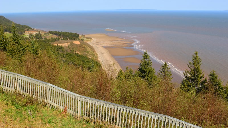 The scene is located within the Fundy Trail Parkway in New Brunswick, Canada, a scenic route featuring secluded beaches and coastal cliffs.
