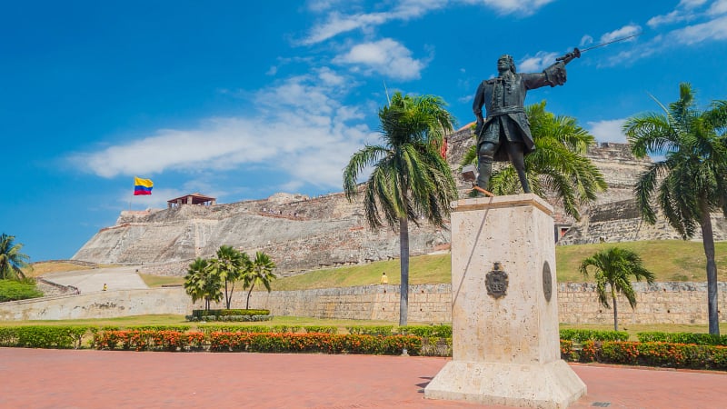 This image features the famous San Felipe de Barajas Fort (Castillo San Felipe de Barajas) in Cartagena de Indias, Colombia, with the prominent bronze Statue of Admiral Blas de Lezo standing on a pedestal in the foreground.