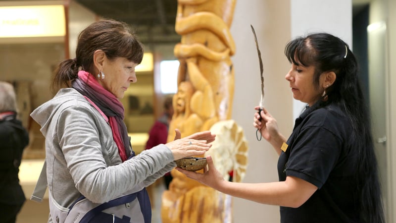 Traditional Indigenous smudging ceremony being conducted inside a museum or cultural center.