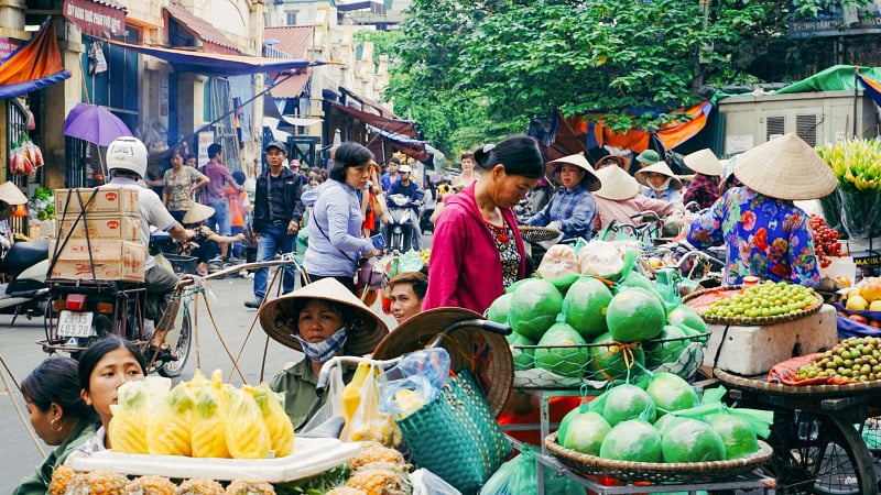 Bustling outdoor street market in Vietnam, likely outside the historic Dong Xuan Market area in Hanoi's Old Quarter.